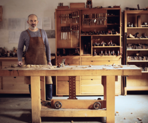 Mężczyzna w pracowni stolarskiej przy stole stolarskim w otoczeniu narzędzi ręcznych